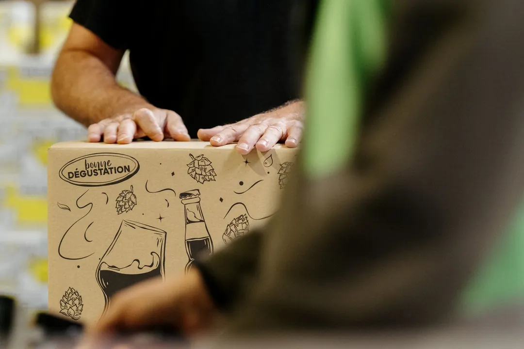 Deux mains posées sur un carton illustré, prêt à être expédié