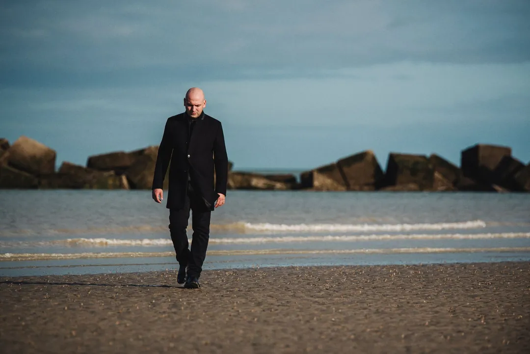 Esteban Fernandez en manteau noir marchant sur une plage