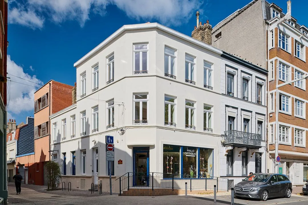 Immeuble d'angle rénové, façade blanche sous un ciel bleu