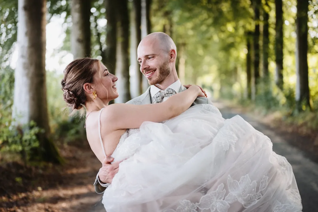 Le marié porte la mariée dans une allée d'arbres