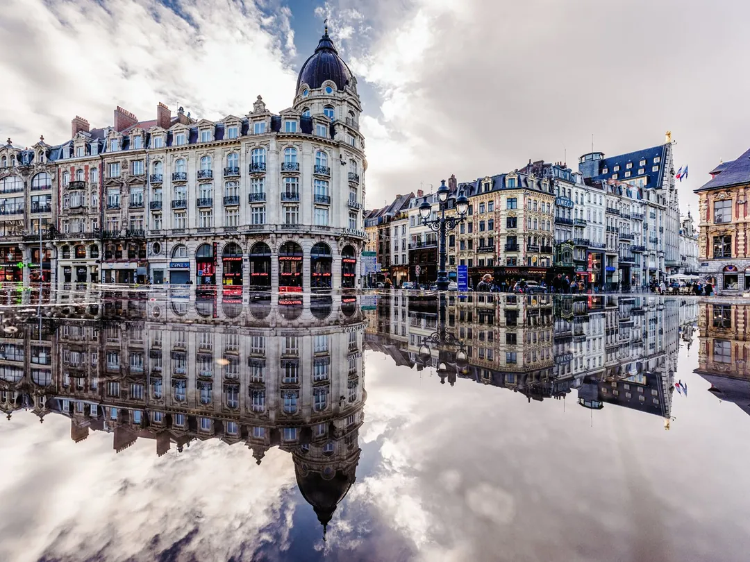 Les façades de Lille reflétées dans une flaque, ciel nuageux