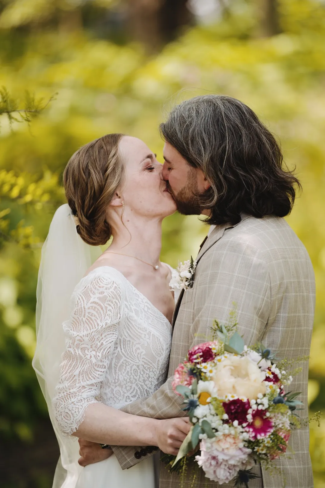 Les mariés s'embrassent, bouquet entre eux