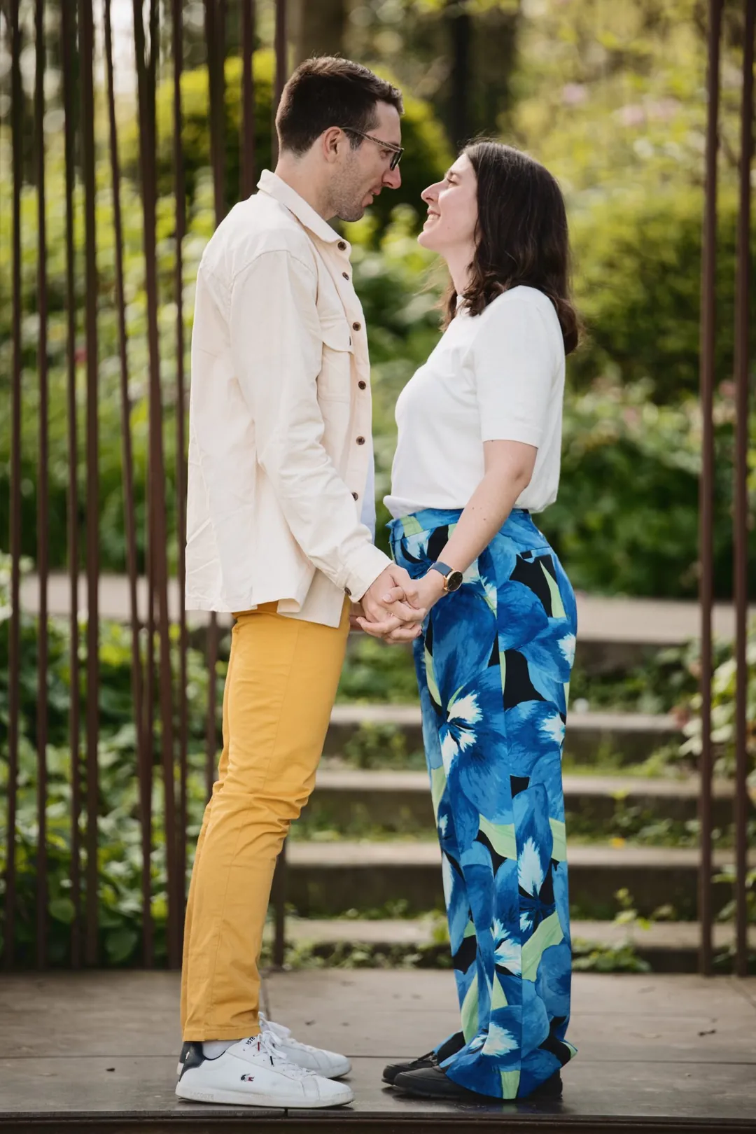 Un couple se regarde devant une grille, dans un jardin
